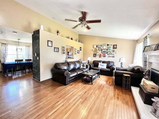 living area featuring light wood finished floors, ceiling fan, lofted ceiling, and a fireplace