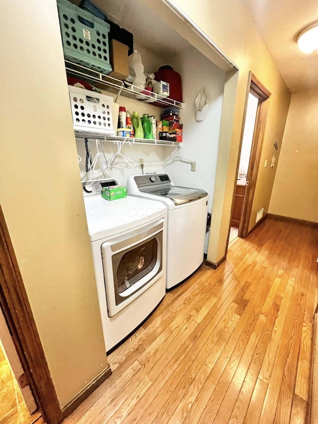 clothes washing area with laundry area, washing machine and dryer, and light wood-type flooring