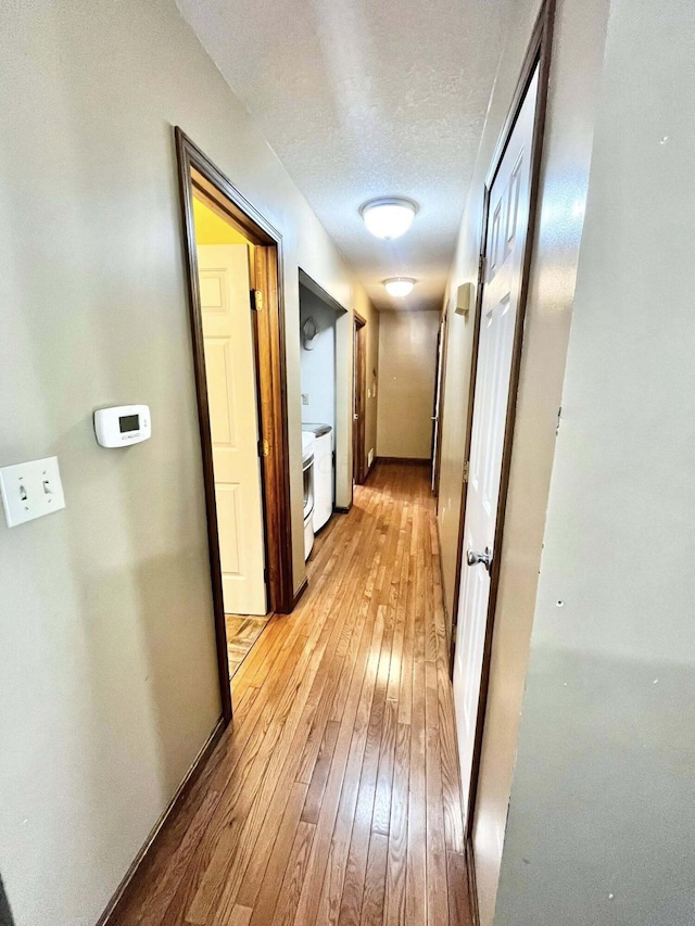 corridor featuring a textured ceiling, baseboards, and light wood-style floors
