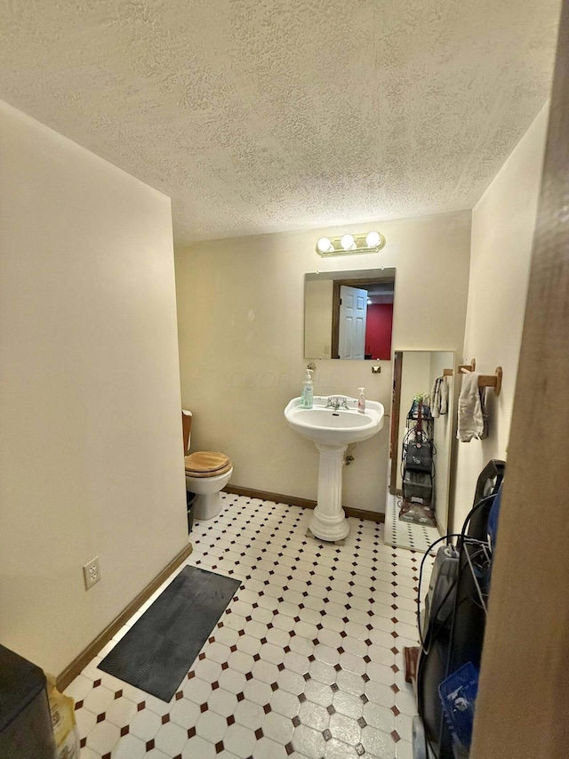 half bath with toilet, baseboards, a textured ceiling, tile patterned floors, and a sink