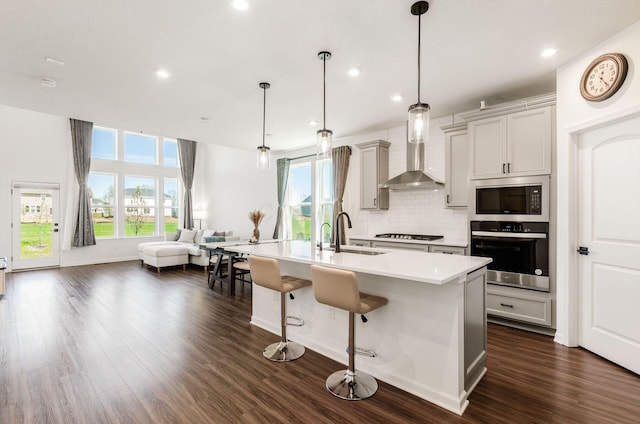 kitchen featuring appliances with stainless steel finishes, a sink, wall chimney exhaust hood, open floor plan, and backsplash