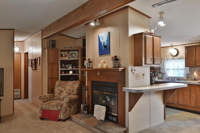 kitchen with brown cabinetry, heating unit, a glass covered fireplace, light carpet, and light countertops