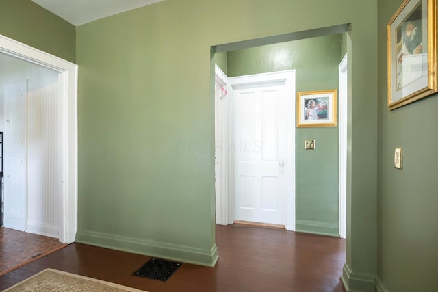 hallway featuring visible vents, baseboards, and dark wood-type flooring