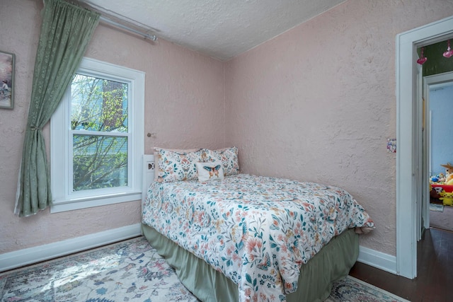 bedroom with baseboards, a textured ceiling, a textured wall, and wood finished floors