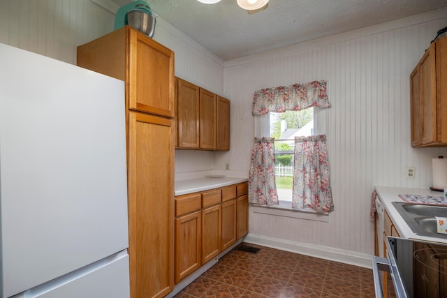 kitchen with light countertops, baseboards, a sink, freestanding refrigerator, and ornamental molding