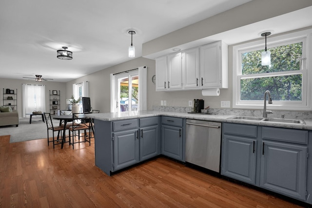 kitchen featuring a peninsula, wood finished floors, a sink, dishwasher, and hanging light fixtures