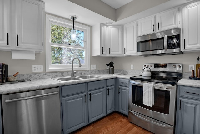 kitchen featuring white cabinets, a sink, gray cabinets, stainless steel appliances, and pendant lighting