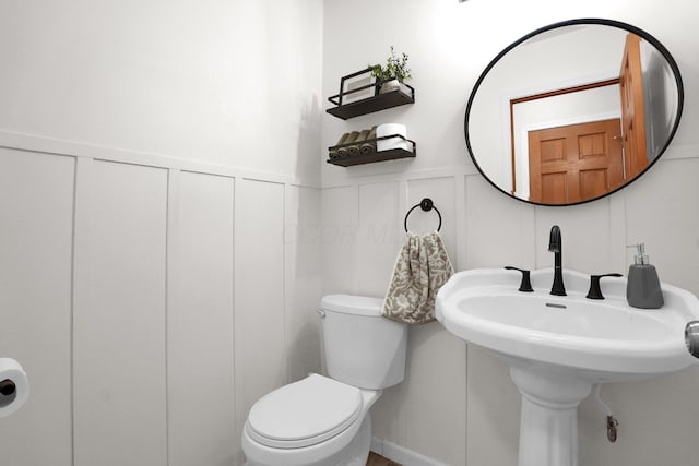 half bath featuring toilet, wainscoting, and a decorative wall