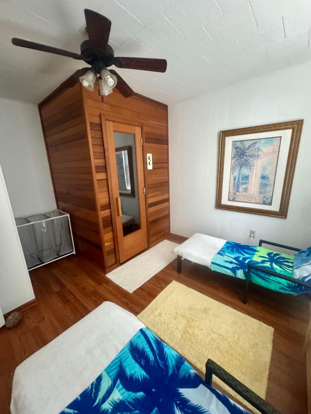 bedroom with wooden walls, ceiling fan, and wood finished floors