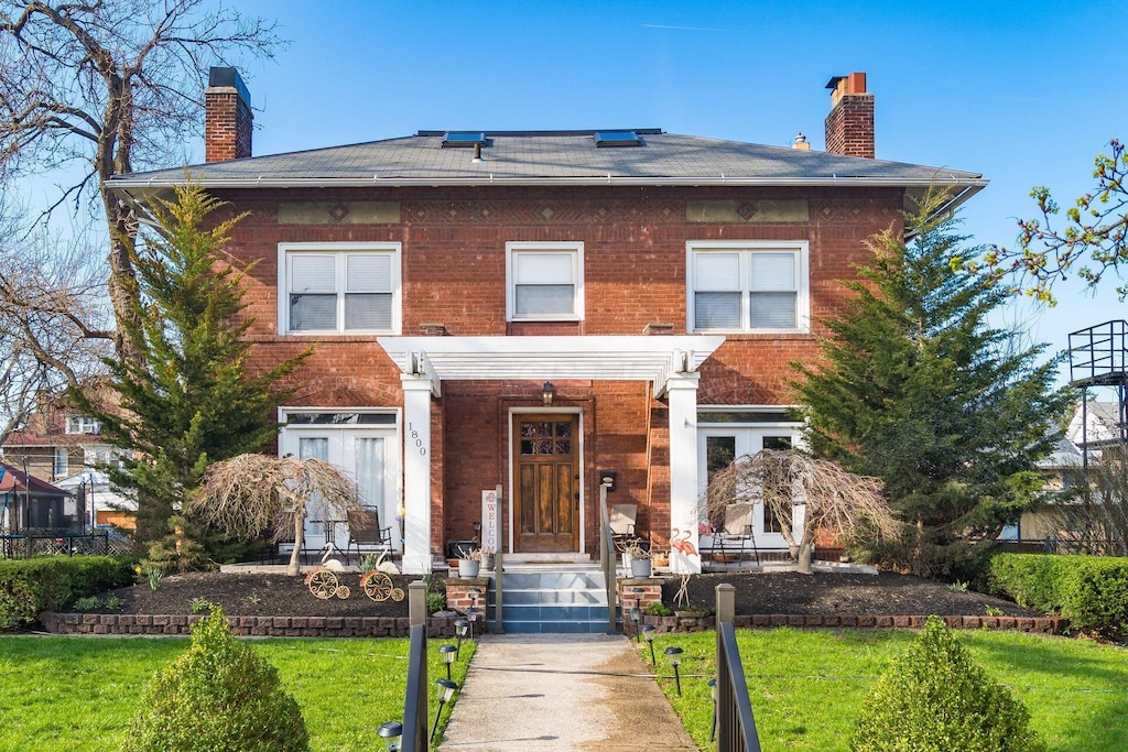 view of front of home featuring brick siding, a front lawn, and a chimney