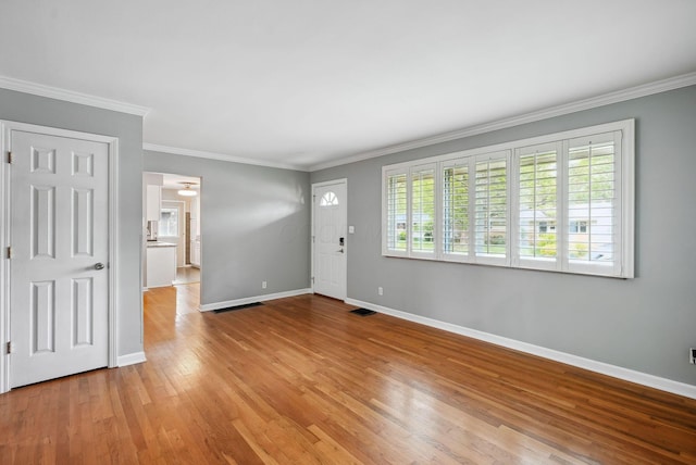 interior space featuring crown molding, baseboards, wood finished floors, and visible vents