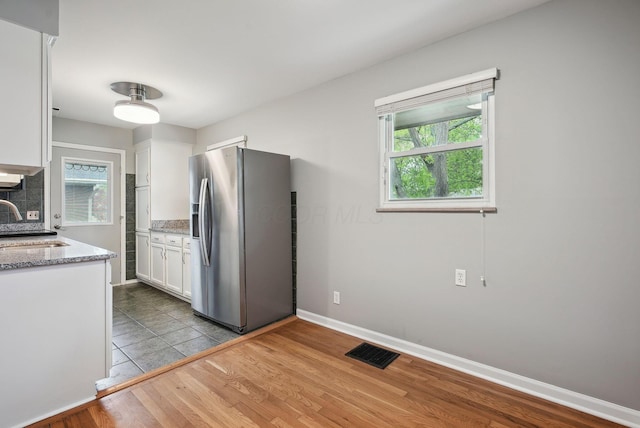 kitchen featuring visible vents, light stone countertops, a sink, stainless steel fridge, and white cabinetry