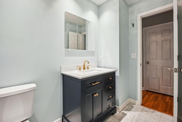 half bath featuring baseboards, marble finish floor, toilet, and vanity
