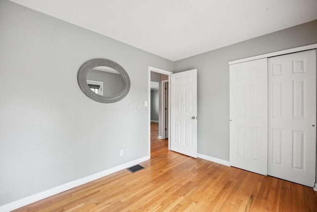 unfurnished bedroom featuring baseboards, light wood-style floors, visible vents, and a closet