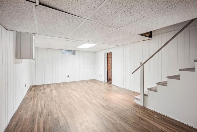 finished below grade area featuring wood walls, a drop ceiling, wood finished floors, and stairway