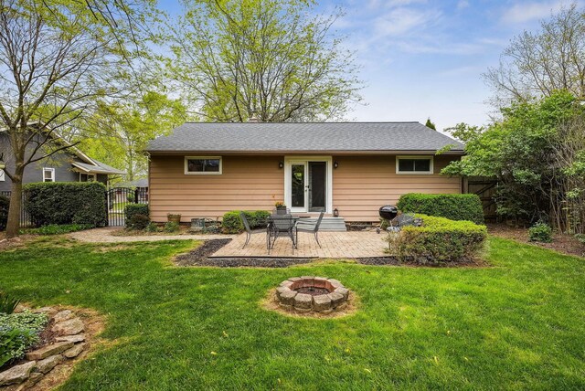 rear view of property with a gate, a fire pit, fence, and a yard
