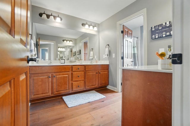 bathroom with double vanity, baseboards, a sink, and wood finished floors