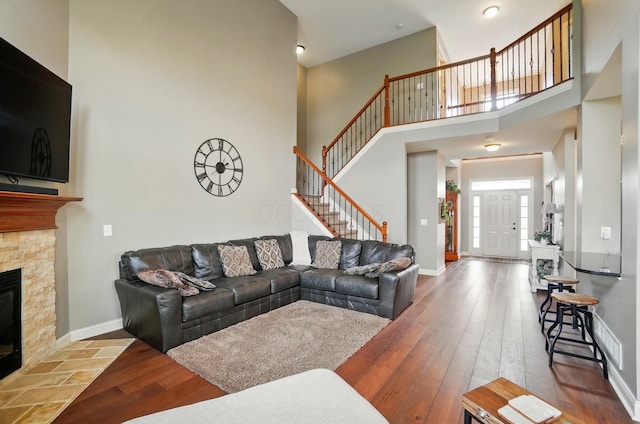 living room with a towering ceiling, a fireplace, hardwood / wood-style flooring, baseboards, and stairs