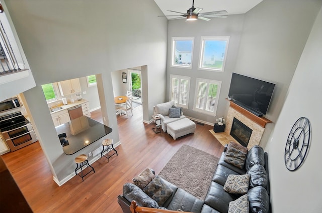 living room with a wealth of natural light, a fireplace, a ceiling fan, and a towering ceiling