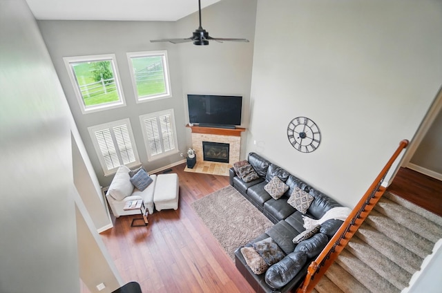 living room featuring a high ceiling, ceiling fan, a fireplace with flush hearth, wood finished floors, and stairway