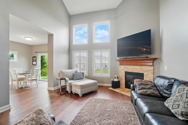 living area with a towering ceiling, baseboards, a fireplace, and hardwood / wood-style floors