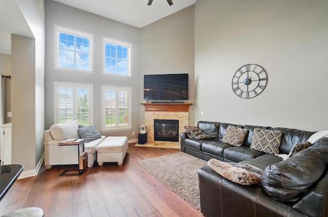 living area with wood-type flooring, a towering ceiling, a fireplace, baseboards, and a ceiling fan