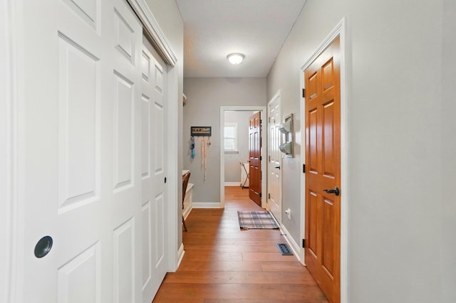 corridor with light wood-style floors, baseboards, and visible vents