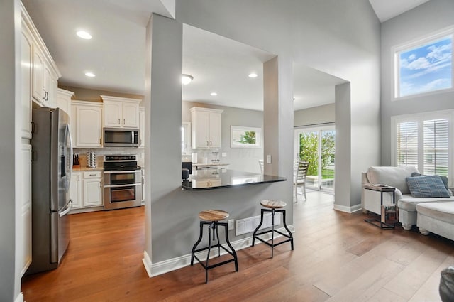 kitchen with light wood finished floors, stainless steel appliances, white cabinetry, a kitchen bar, and backsplash