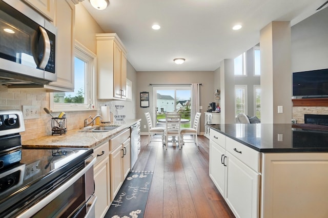 kitchen with appliances with stainless steel finishes, a sink, dark stone countertops, dark wood-type flooring, and backsplash