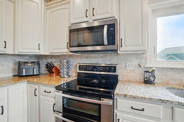 kitchen featuring appliances with stainless steel finishes, light stone countertops, backsplash, and white cabinetry