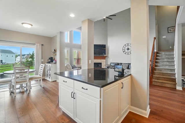 kitchen with a stone fireplace, wood-type flooring, open floor plan, recessed lighting, and white cabinetry
