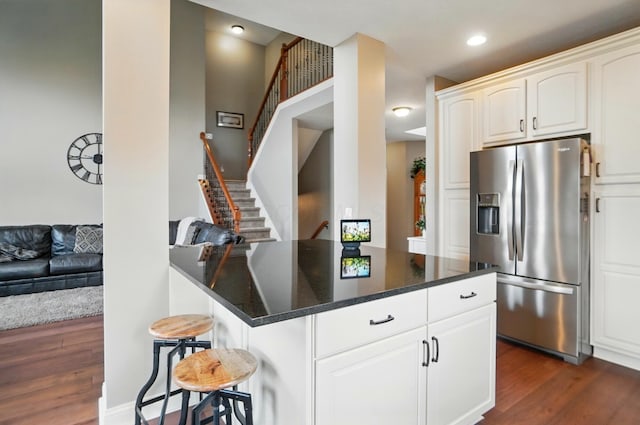 kitchen with a breakfast bar area, stainless steel refrigerator with ice dispenser, dark stone counters, white cabinets, and dark wood finished floors