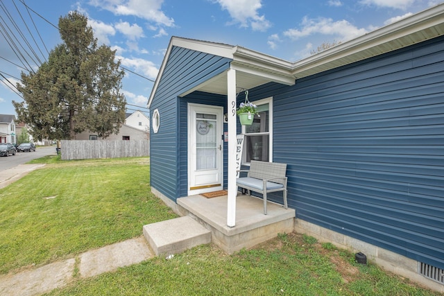 view of exterior entry featuring fence and a yard