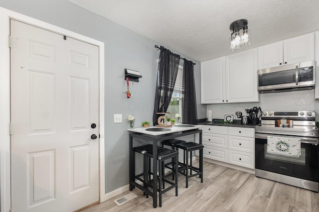 kitchen with a textured ceiling, stainless steel appliances, white cabinetry, light wood-type flooring, and visible vents