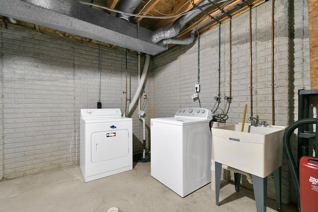 washroom with independent washer and dryer, brick wall, a sink, and laundry area