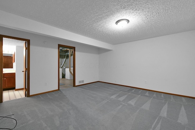 finished below grade area featuring carpet flooring, a textured ceiling, visible vents, and baseboards