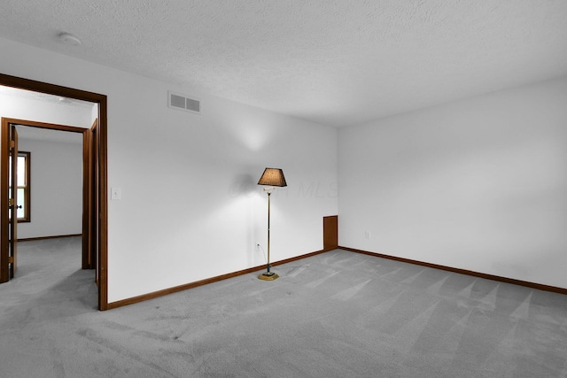 spare room with carpet floors, baseboards, a textured ceiling, and visible vents