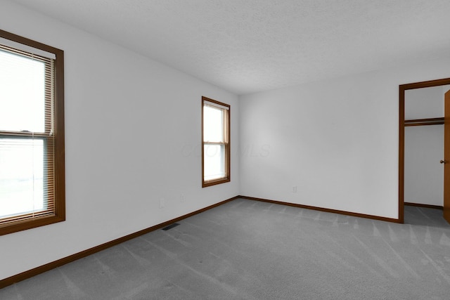 carpeted empty room featuring baseboards, a textured ceiling, and visible vents