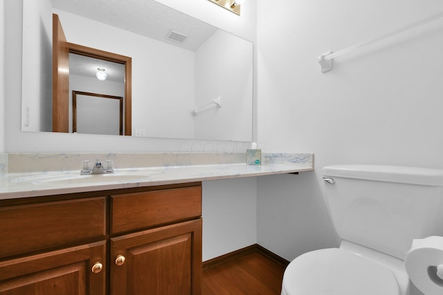 bathroom with visible vents, vanity, wood finished floors, toilet, and baseboards