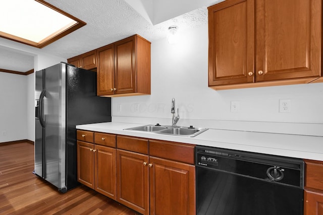 kitchen with brown cabinets, a sink, light countertops, black dishwasher, and wood finished floors
