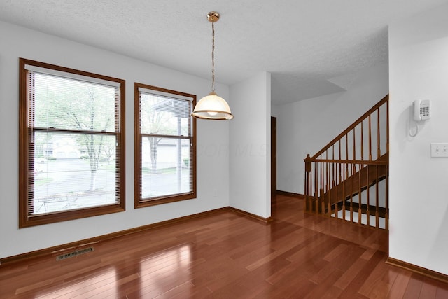 unfurnished dining area featuring visible vents, baseboards, stairs, and wood finished floors