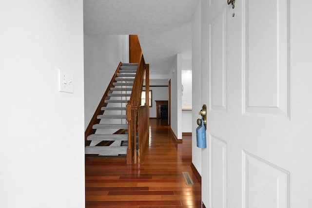 entryway with a textured ceiling, visible vents, wood finished floors, stairway, and baseboards