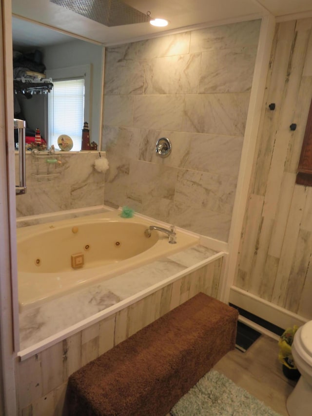 bathroom with toilet, a tub with jets, and wood finished floors