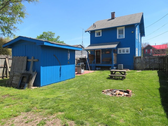rear view of property with a fenced backyard, an outdoor structure, a yard, and an outdoor fire pit