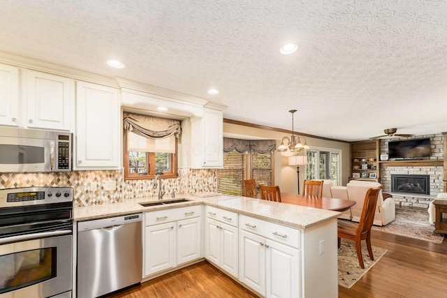 12385 Woodsfield Cir E, Pickerington, OH 43147 - kitchen with appliances with stainless steel finishes, a sink, a fireplace, a textured ceiling, and a peninsula