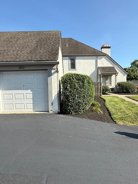 302 Saint Andrews Dr Unit 302, Dublin, OH 43017 - view of home's exterior featuring roof with shingles, a chimney, an attached garage, driveway, and stucco siding