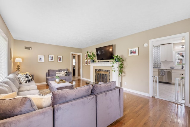 living room featuring light wood-style floors, baseboards, a glass covered fireplace, and visible vents