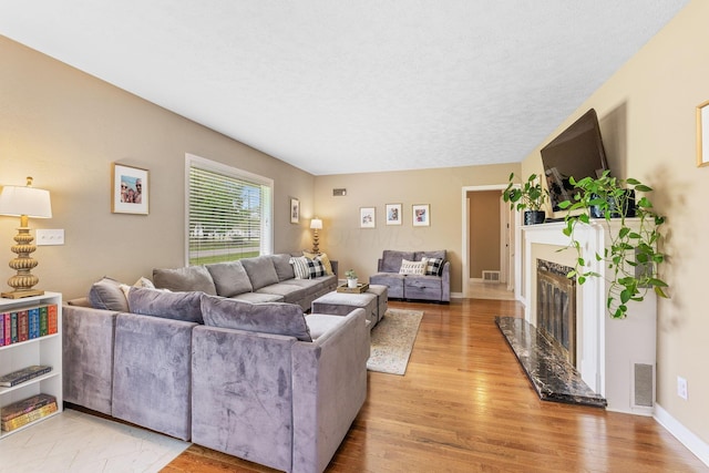 living room featuring visible vents, a textured ceiling, light wood finished floors, and a fireplace