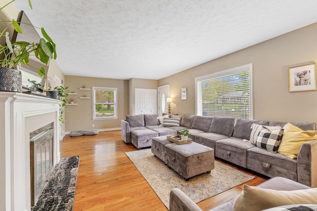 living area with a premium fireplace, a textured ceiling, baseboards, and light wood-style floors