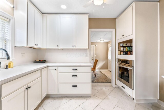 kitchen with light countertops, white cabinetry, stainless steel oven, and ceiling fan